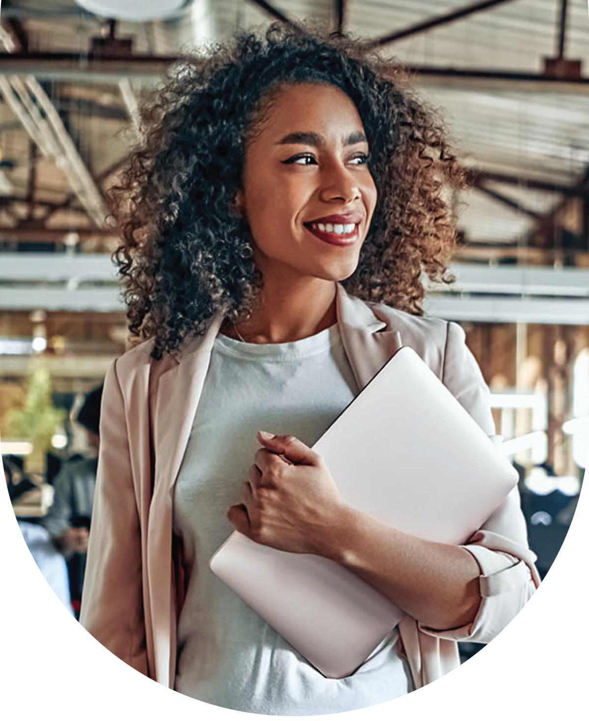 Woman with dark curly hair holding a laptop in an office